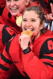 Jamie Lee Rattray posing for a team photo for Team Canada and biting into her gold medal