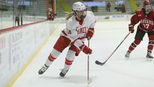 Jamie Bourbonnais skating down the boards with the puck with a Harvard University player behind her