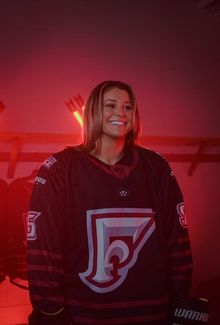 Headshot of Sam Isbell in her hockey gear with a dark red moody background