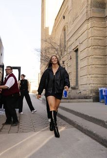 Kayle Osborne walking away from the team bus in a stylish all black outfit and knee-high black boots.