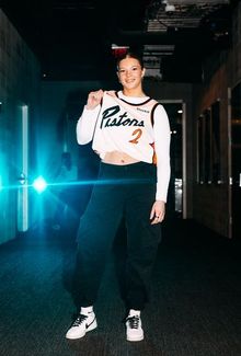 Kayle Osborne holding up Detroit Pistons #2 jersey in dimly lit hallway with teal lighting.