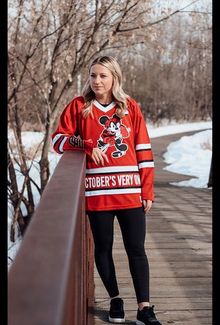 Savannah Harmon in a red hockey jersey standing on a bridge and looking off into the distance