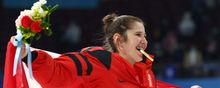 Jamie Lee Rattray smiling and celebrating the Team Canada gold medal win with a Canada flag held behind her back