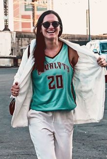 Jill Saulnier in the arena parking lot smiling and flashing her coat open to reveal a basketball jersey