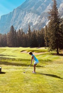 Victoria Bach playing golf on a golf course with mountains in the background.