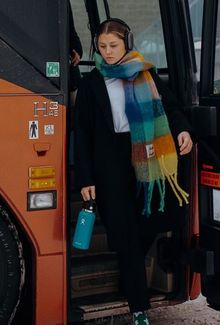 Sam Isbell walking off the team bus in a black outfit, large colorful scarf, and over ear headphones