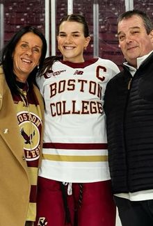 Abby Newhook posing for a photo with her parents on the ice in her Boston College gear.