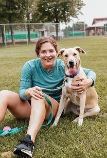 Nicole Hensley sitting in the grass and hugging her dog